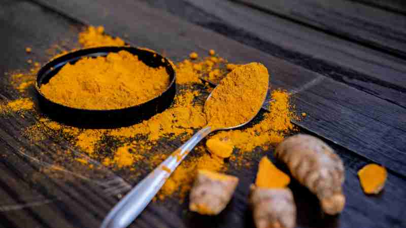 Vibrant turmeric powder and root on a dark wooden surface, emphasizing natural spices., tags: und - pexel