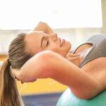 A woman in a gym smiling while exercising on a stability ball. Fitness and positivity., tags: junkfood - pexel