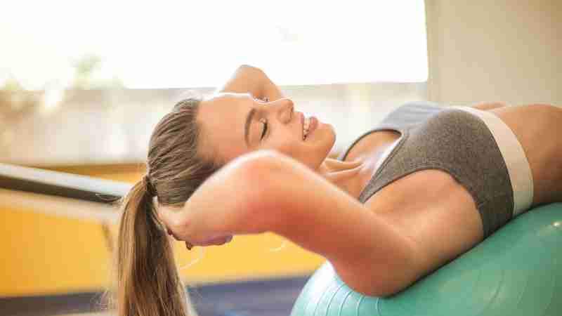 A woman in a gym smiling while exercising on a stability ball. Fitness and positivity., tags: junkfood - pexel