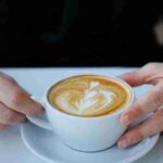 Close-up of a latte art coffee held by a person wearing rings at a cafe., tags: kaffee - pexel
