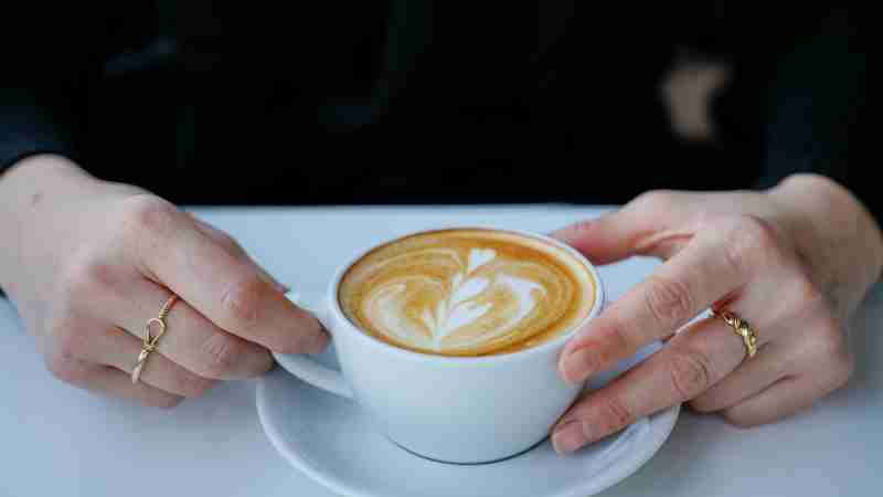 Close-up of a latte art coffee held by a person wearing rings at a cafe., tags: kaffee - pexel